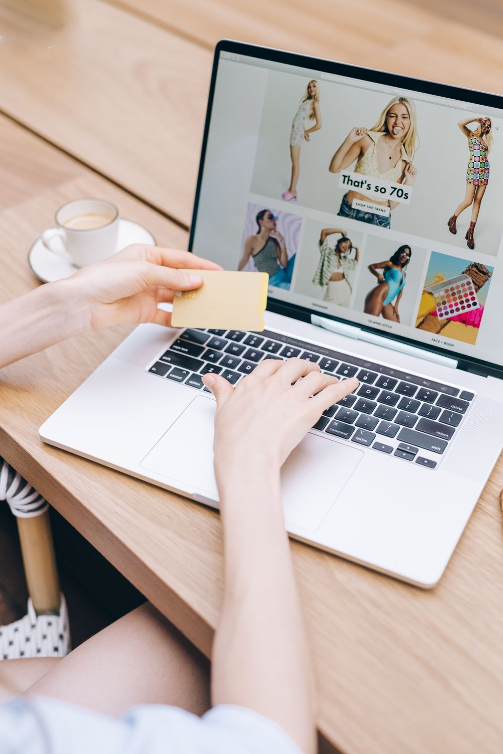 Hands holding a card beside a laptop at a wooden table